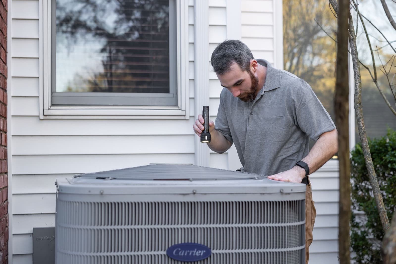 HVAC technician performing spring AC maintenance on an outdoor unit